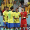 Two national football teams, Brazil and Morocco, celebrating their qualification for the World Cup playoffs. The Brazilian team is wearing yellow jerseys and the Moroccan team is wearing red jerseys. They are embracing and smiling. The background shows a stadium with cheering fans.