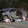 A photorealistic image depicting a devastating car accident scene. A damaged car is shown with debris scattered around. Several children are visible, some appearing injured or lifeless, near the wreckage. The setting is a rural road with trees in the background. Focus on conveying the tragedy and loss of life.