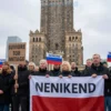 A dramatic, wide-angle photograph depicting a solemn scene in Warsaw, Poland. The image should show a group of Polish citizens holding signs and banners protesting the renaming of historical monuments. The atmosphere should be serious and respectful, with a focus on the emotional impact of the issue. The background should feature the city's architecture, emphasizing its historical significance.