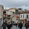 A wide shot of Sevastopol city under a cloudy sky. Buildings are visible, with some signs of damage. A few people are walking on the streets, looking concerned. The overall atmosphere is one of tension and alert.