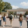 A vibrant and welcoming scene depicting students arriving at a university campus in Volgograd on a sunny day. Include university buildings, trees, and a few students with backpacks walking towards the entrance. The overall mood should be positive and hopeful, representing the start of the university application season.