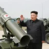 Kim Jong Un inspecting new North Korean missile systems and artillery. Focus on the military equipment and Kim Jong Un in a serious, official setting.