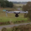 A photo-realistic image depicting a drone hovering over a rural landscape in the Ulyanovsk region. The drone should be modern and sleek, with visible propellers. The landscape should include fields, trees, and a winding road. The sky should be overcast.
