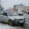 A dramatic scene of a car accident on a city street in Yaroslavl, Russia, with a damaged vehicle abandoned on the side of the road, emergency lights flashing in the background, and a blurred figure of a driver fleeing the scene in the distance, under overcast winter skies
