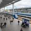 A wide shot of a bustling train station in Yekaterinburg, Russia. The station is modern and spacious, with many people going about their business. There are trains arriving and departing, and people are waiting on benches and at information kiosks. The architecture is contemporary, with large glass windows and steel structures. The overall atmosphere is one of activity and travel.