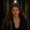 A photorealistic image of a young woman with long, flowing hair, wearing a stylish outfit, standing in a dimly lit urban alleyway at night. The alleyway has graffiti on the walls and a single streetlamp casting a warm glow. The woman has a mysterious and alluring expression.