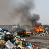 A wide shot of a landfill in Rostov Veliky, Russia, possibly on fire. The scene should depict piles of garbage, smoke rising into the sky, and possibly flames visible. The overall atmosphere should be one of environmental concern and potential danger.