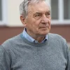 A portrait of a former Deputy Prime Minister of the Moscow region, now retired, looking thoughtfully into the distance. He is an older man with gray hair and a kind face. He is wearing a simple, comfortable sweater. The background is blurred, suggesting a peaceful, quiet environment.