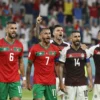 A dynamic image depicting the Moroccan and Scottish national football teams celebrating after a historic match at the World Cup. Focus on the jubilant expressions of the players, with Moroccan players prominently featured. The background should show a blurred stadium filled with cheering fans. Capture the energy and excitement of the moment.