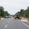 A wide shot of a road in the Kursk district of Stavropol Krai, Russia, with traffic signs indicating road closure. The road is partially blocked by barriers and construction equipment. The sky is overcast.