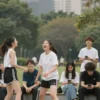 A diverse group of young people (ages 16-25) are shown in a vibrant, modern city park. They are engaged in various activities – some are laughing and talking, others are playing frisbee, and a few are sitting on a bench, looking at their phones. The overall mood is joyful and energetic. Focus on capturing the diversity of ethnicities and body types within the group.