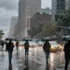 A stormy urban landscape in New York City with heavy rain, strong winds, and flooded streets, showing people with umbrellas walking cautiously, cars driving slowly through water, and dark clouds overhead, conveying a sense of severe weather warning