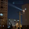 A nighttime view of the residential complex "Akvarel" in Rostov, Russia, with power lines visibly damaged and sparking. The scene depicts the aftermath of an accident causing a power outage. Focus on the damaged infrastructure and the darkened buildings.