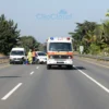 A modern, brightly lit highway with multiple lanes and a clear view of a large, imposing emergency services vehicle (ambulance/fire truck) approaching a scene of a minor traffic accident. The accident scene should be minimal, showing only a few damaged vehicles and emergency responders attending to the situation. Focus on conveying a sense of efficiency and resolution.
