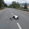 Debris from a crashed drone scattered on a road in Sochi, with surrounding urban landscape, asphalt surface, and faint signs of emergency response activity, no people visible