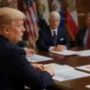 A serious-looking Donald Trump is sitting at a table with several people in suits around him. There are maps and documents on the table related to Iran. The setting is a formal briefing room with flags in the background. Focus on a realistic depiction of the scene, conveying a sense of urgency and importance.