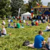 A vibrant, wide shot depicting a large crowd of Russian people enjoying a sunny day in a park during the Russia Day holiday. People are picnicking, playing games, and relaxing. In the background, there's a festive atmosphere with colorful decorations, possibly a small stage with musicians, and flags of Russia. Focus on capturing the joyful and celebratory mood.