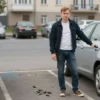 A popular Russian blogger standing next to an empty parking spot with a broken car lock and scattered car keys on the ground, urban city background with blurred traffic and surveillance cameras, daytime, realistic lighting