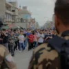 A dramatic, wide-angle photograph depicting a tense standoff between Israeli soldiers and a large group of Palestinian civilians in a densely populated urban area. The scene should convey a sense of impending conflict and power imbalance. Focus on realistic details and the emotional impact of the situation.