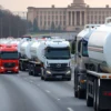 A fleet of fuel tankers driving on a highway in the Ulyanovsk region, with a government building visible in the background. Focus on the trucks and the road, conveying a sense of logistical operation.