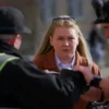 A woman courier in a Гагаринский район (Gagarin district) in Moscow, Russia, being apprehended by police officers. The scene should depict a street setting with buildings in the background. Focus on the arrest and the courier's expression.