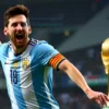 Lionel Messi celebrating a goal during a FIFA World Cup match, wearing the Argentina national team jersey, with the World Cup trophy subtly in the background. Focus on his jubilant expression and dynamic pose. The stadium lights should be visible but not overpowering.