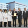 A group of doctors in formal attire are receiving awards on a stage. The background features a blurred image of a modern hospital building. The atmosphere is celebratory and professional. Focus on the doctors' expressions of pride and accomplishment.
