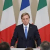 Italian Prime Minister Giorgia Meloni addressing a press conference, stern expression, surrounded by Italian flags and reporters. The scene should convey a sense of seriousness and political tension.