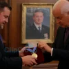 A formal room in Poland. A Polish official is carefully placing a medal onto a velvet cushion. In the background, a portrait of Volodymyr Zelenskyy is subtly visible, slightly out of focus. The atmosphere is serious and respectful.