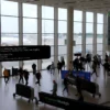 A busy Munich airport terminal with airplanes on the runway, travelers moving through the terminal, and a large digital display showing flight information, captured in a realistic style