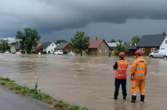 A river flooding in the town of Revda, with water rising near houses and roads, emergency personnel monitoring the situation, dark stormy skies, and no people in danger or visible distress
