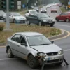 A damaged foreign car on a roundabout in Rostov-on-Don after a traffic accident. The car should be visibly wrecked, with damage to the front end. The roundabout should be a typical urban roundabout with traffic lights and road markings. Include other vehicles in the background, showing the aftermath of the accident.