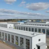 A wide shot of several food processing plants in the Smolensk region of Russia. The plants are modern and well-maintained, with large windows showing activity inside. A clear blue sky with some clouds is visible in the background. Focus on the buildings and the overall industrial landscape.