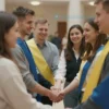 A warmly lit, medium shot of a diverse group of people (representing Russian and Ukrainian citizens) standing together, smiling, and holding hands. They are in a modern, welcoming setting, perhaps a government building or a cultural center. The atmosphere should be one of unity and friendship.