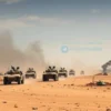 A dramatic scene showing a Russian military vehicle convoy moving through a desert landscape in Iraq, with visible signs of conflict such as smoke rising from distant explosions and abandoned defensive positions, but without any text, symbols, or graphic violence