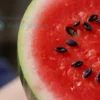 A close-up, photorealistic image of a ripe watermelon, showing its vibrant red flesh and black seeds. The watermelon should be slightly cut open to reveal the interior. The background should be blurred, suggesting a summer setting.