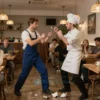 A plumber and a chef are fighting in a cozy downtown Moscow cafe, with broken dishes on the floor, customers reacting in shock, and traditional Russian interior details like wooden tables and warm lighting, no text or numbers