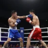A dynamic, wide shot of a boxing match taking place in a large, brightly lit indoor arena. Two boxers are in the ring, mid-action, with one throwing a punch. The crowd is blurred in the background, showing excitement and energy. Focus on the boxers' faces and the intensity of the moment.