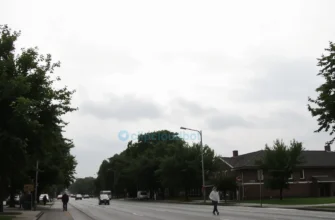 A cloudy, overcast day in Smolensk on June 27th, with soft diffused light, gray skies, and a quiet urban landscape featuring tree-lined streets, modest brick buildings, and people walking with light jackets, no sun visible, calm atmosphere