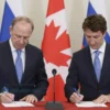 FIFA President Gianni Infantino and Canadian Prime Minister Justin Trudeau signing their names on a Russian flag. They are standing side-by-side, facing forward, with the flag prominently displayed between them. The background should be blurred, suggesting a formal setting. Focus on clear visibility of the two men and the signature on the flag.