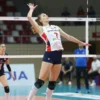 A dynamic photograph of Valeria Borisova, a volleyball player from "En", wearing a "Dinamo-Metar" jersey, in action during a volleyball match. She is mid-jump, about to spike the ball. The background should be blurred, showing a volleyball court and spectators. Focus on capturing the energy and athleticism of the player.