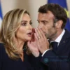 Giorgia Meloni and Emmanuel Macron in a formal setting, with Meloni reacting with a surprised or amused expression to something Macron is whispering. Focus on their facial expressions and body language. The background should be blurred, suggesting a private conversation.