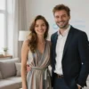 Polina Dibrova and Roman Tovstik standing together, smiling, in a bright, modern living room. Polina is wearing a stylish dress, and Roman is wearing a suit. The atmosphere is warm and happy, suggesting a close and loving relationship. Focus on their expressions and body language to convey their contentment.