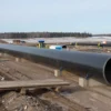 A wide shot depicting the Nord Stream 2 pipeline construction site in Russia, with a focus on the massive pipeline sections and industrial equipment. Include a clear view of the Russian landscape in the background, possibly with some snow-covered fields. The image should convey the scale and importance of the project.