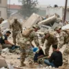 A wide shot depicting US military personnel assisting in the aftermath of an earthquake in a devastated urban area. Soldiers are shown clearing rubble, providing aid to survivors, and securing the scene. The scene should convey a sense of urgency and humanitarian effort. Focus on the interaction between the military personnel and the affected civilians.