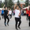 A group of diverse students in a vibrant, celebratory flash mob in a public square in Volgograd, Russia. They are performing a choreographed dance, expressing joy and unity. The scene should capture the energy and spirit of the event, with a focus on the students' expressions and the colorful clothing they are wearing. The background should include recognizable Volgograd landmarks subtly visible.