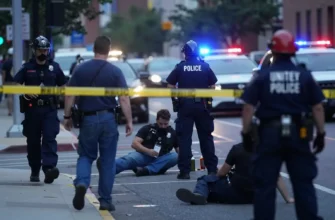 A chaotic urban scene in the United States with multiple people on the ground, emergency responders arriving, and police tape cordoning off an area, all under dim daylight with distant sirens visible, no weapons or blood shown