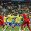 A dramatic scene of the Brazil vs. Morocco match at the 2026 World Cup. Focus on the intensity of the game, with players from both teams in action. Include a large stadium filled with spectators, showcasing the excitement of the event. The Brazilian team should be wearing their iconic yellow jerseys, and the Moroccan team in their red jerseys. Capture the moment of the match, emphasizing the struggle and determination of both sides.