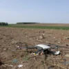 A rural landscape in Krasnodar Krai with debris from a downed drone scattered on the ground, surrounded by fields and distant trees, under a clear sky, no people visible