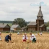 A serene landscape depicting a traditional Russian village scene on June 24, 2026. Focus on elements associated with folk traditions and nature. Include fields of wheat, a wooden church, and villagers engaged in peaceful activities like harvesting or crafting. The overall mood should be calm and reflective, representing the customs and beliefs associated with the day.